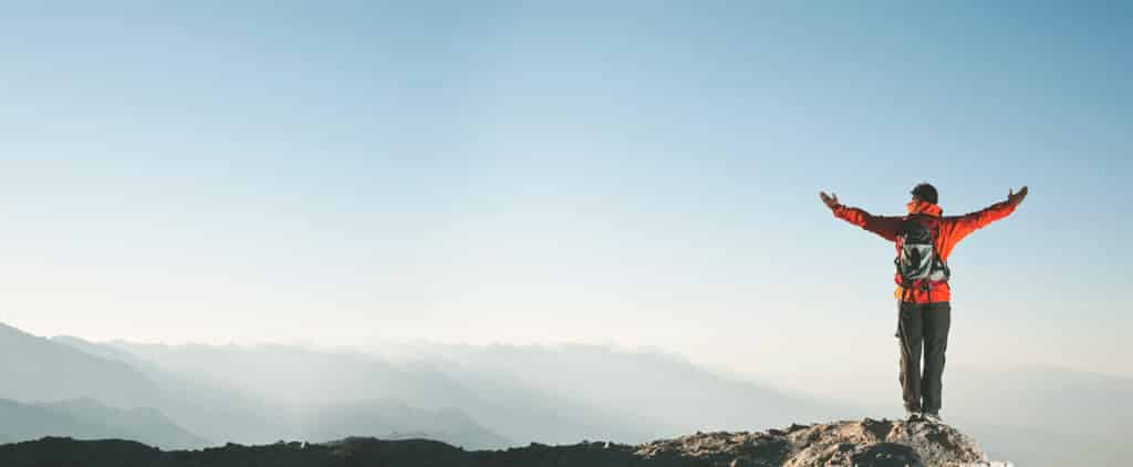 person on the top of a mountain raising their hands up