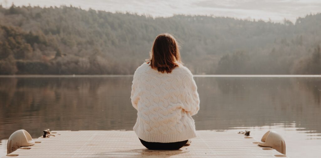 A woman is sitting on a dock next to a lake presumably wondering if Effexor can cause addiction and withdrawal.