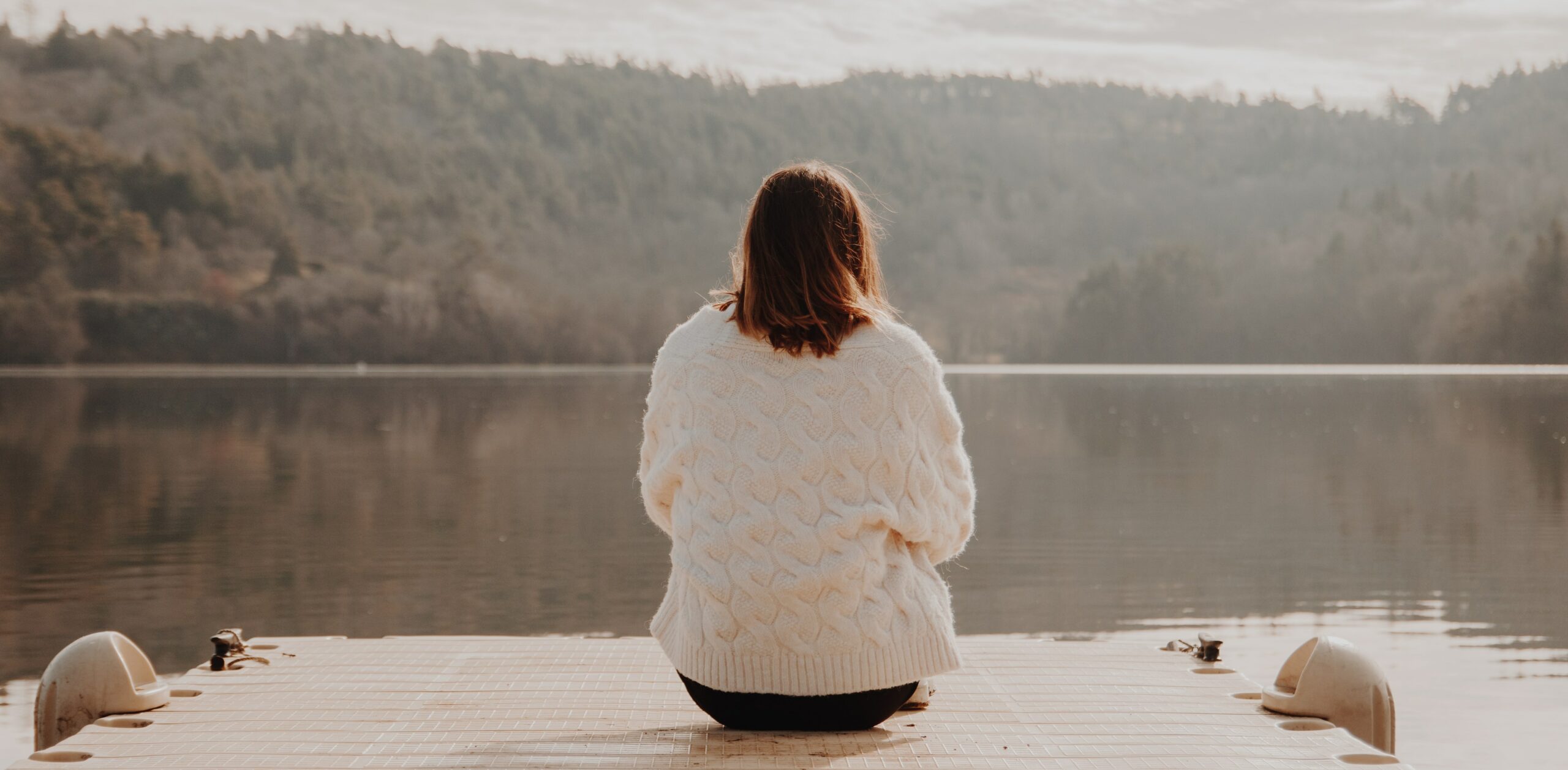 A woman is sitting on the beach of a lake to represent Prescription Drug Detox & Withdrawal Treatment.