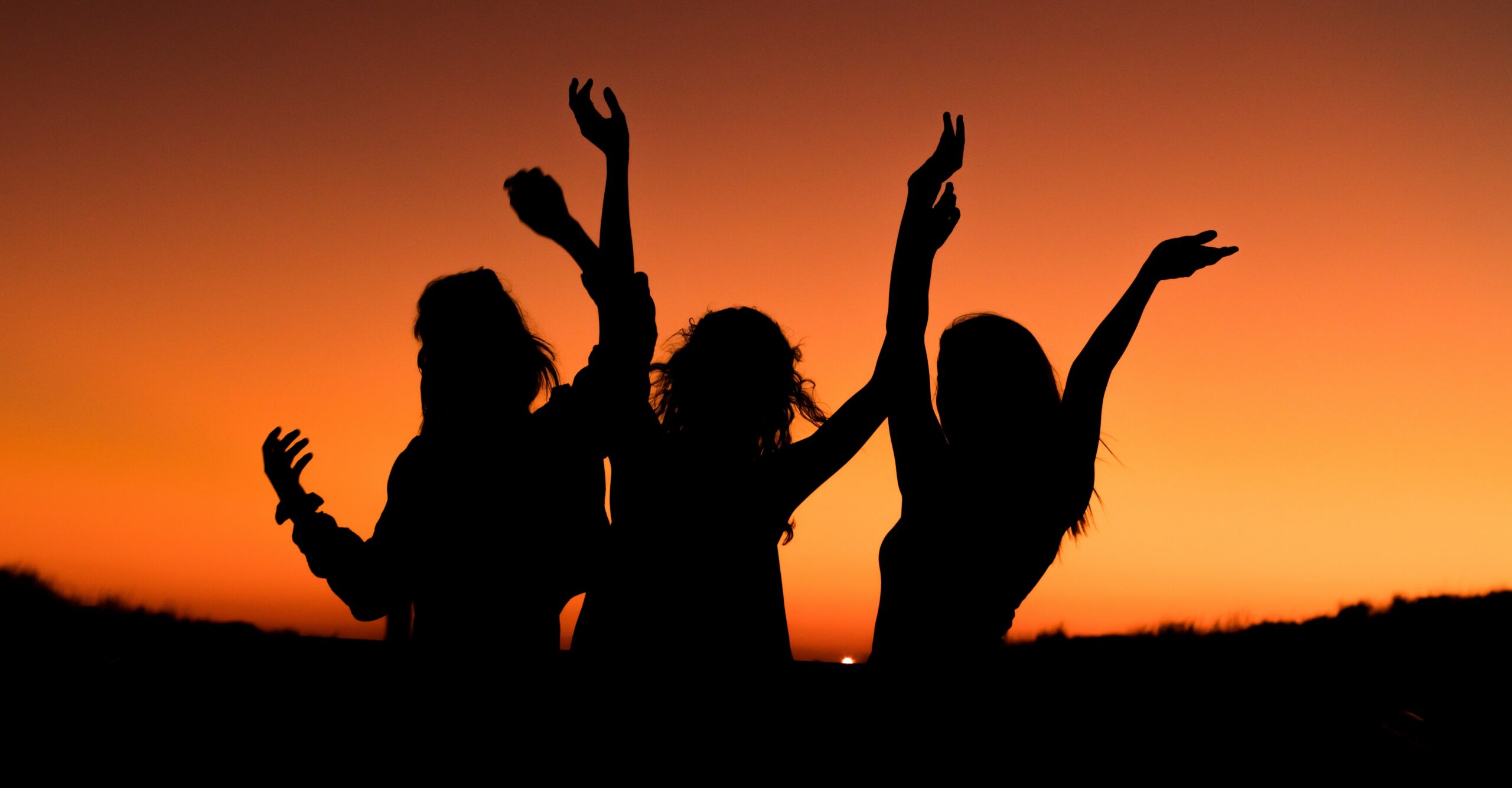 Three people are shadowed with their hands up in celebration against a sunset representing best sober nightlife activities to do in newport beach california.