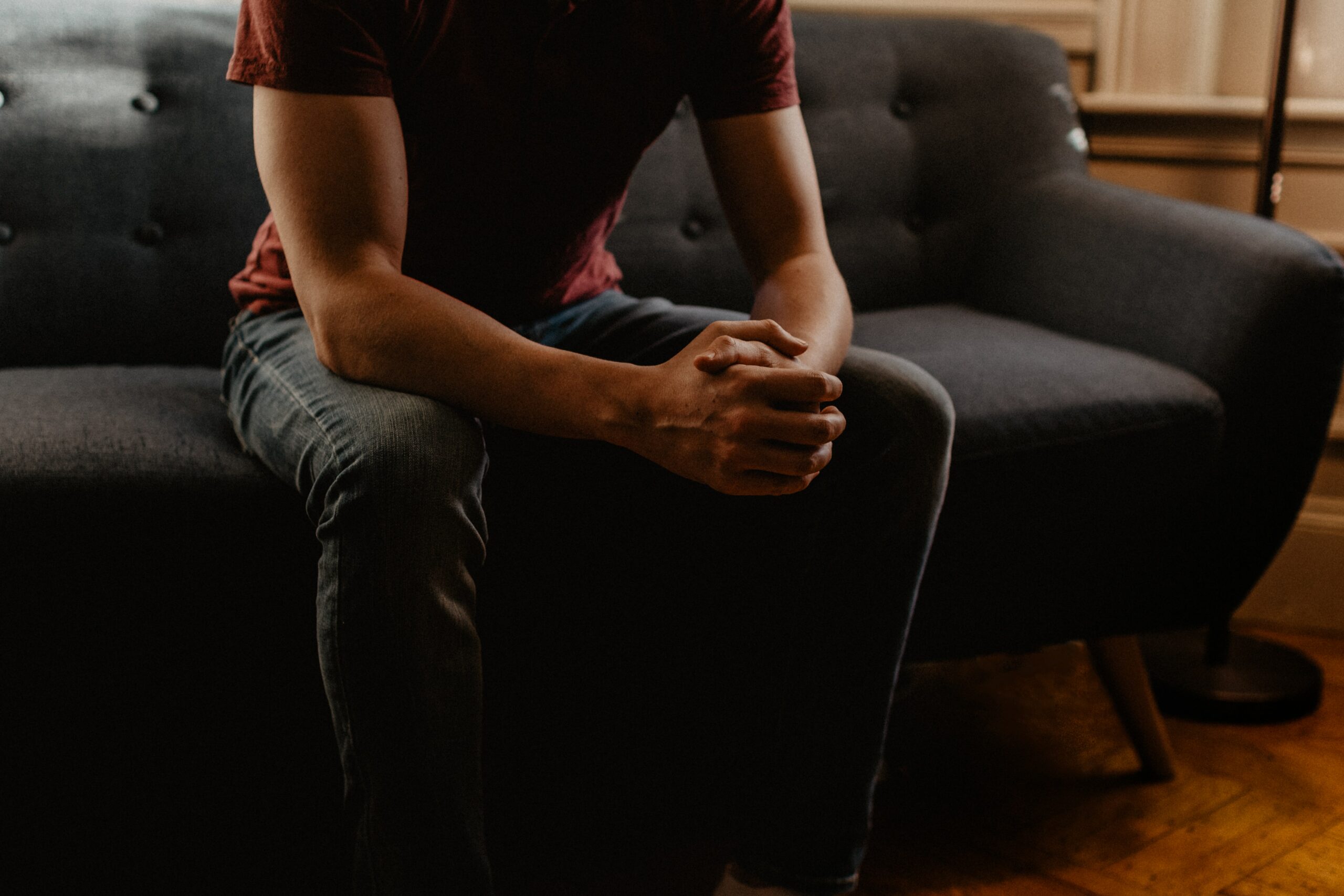 bottom half of a person sitting on a couch with their hands together in their lap