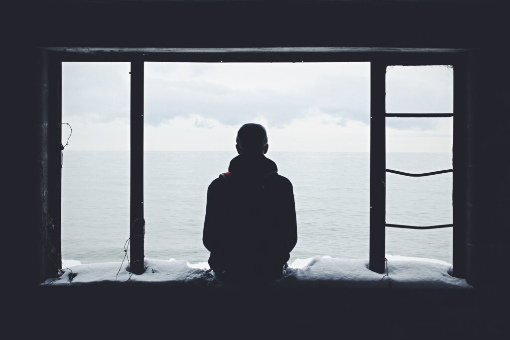 a man sits in front of a window to represent Prescription Drug Detox & Withdrawal Treatment.