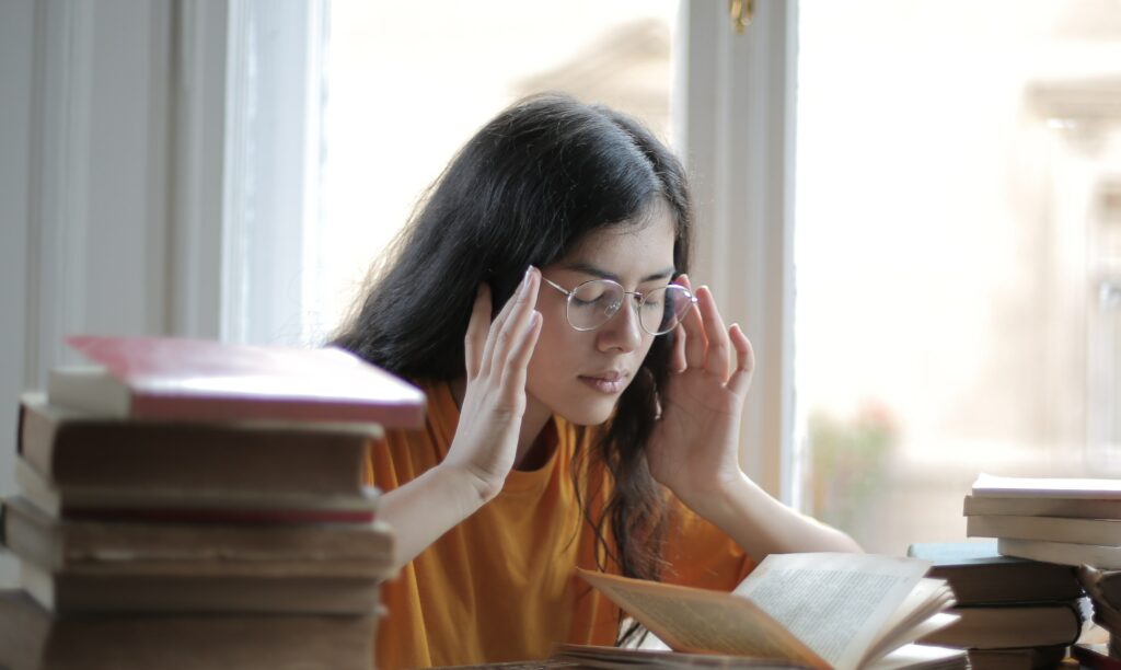 a woman sits at a desk with her hands rubbing her temples to represent barbiturate addiction treatment. .