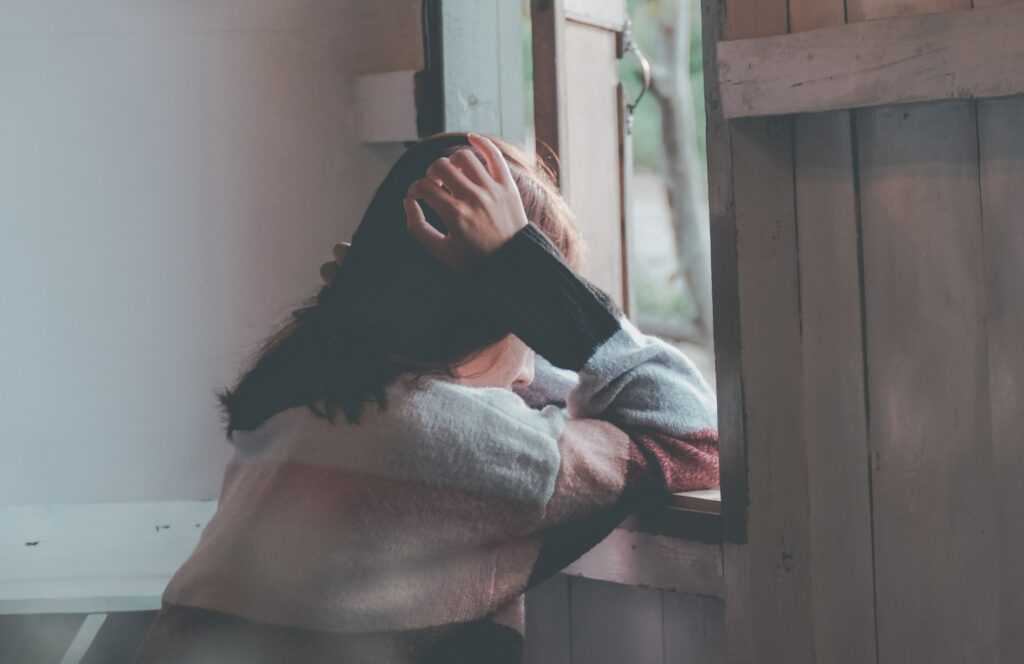 a woman is looking out a window to represent signs of adderall addiction.