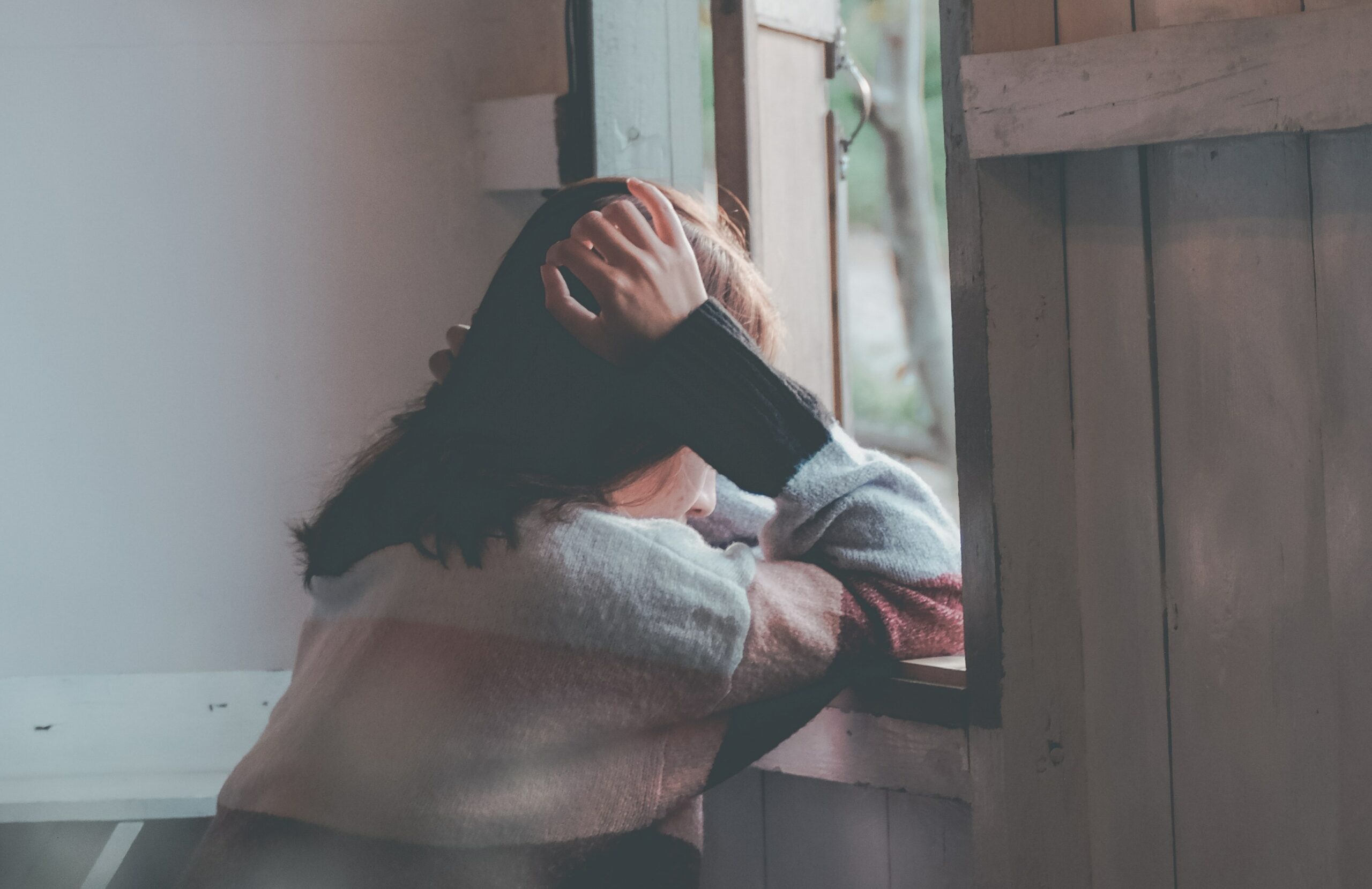 a woman sits looking out a window to represent kratom withdrawal rehab in california.