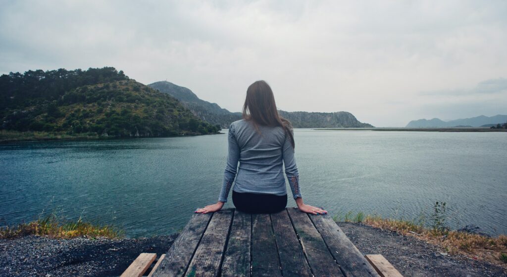 a woman is sitting on a dock looking out at the lake to represent the question is gabapentin addicting in california.