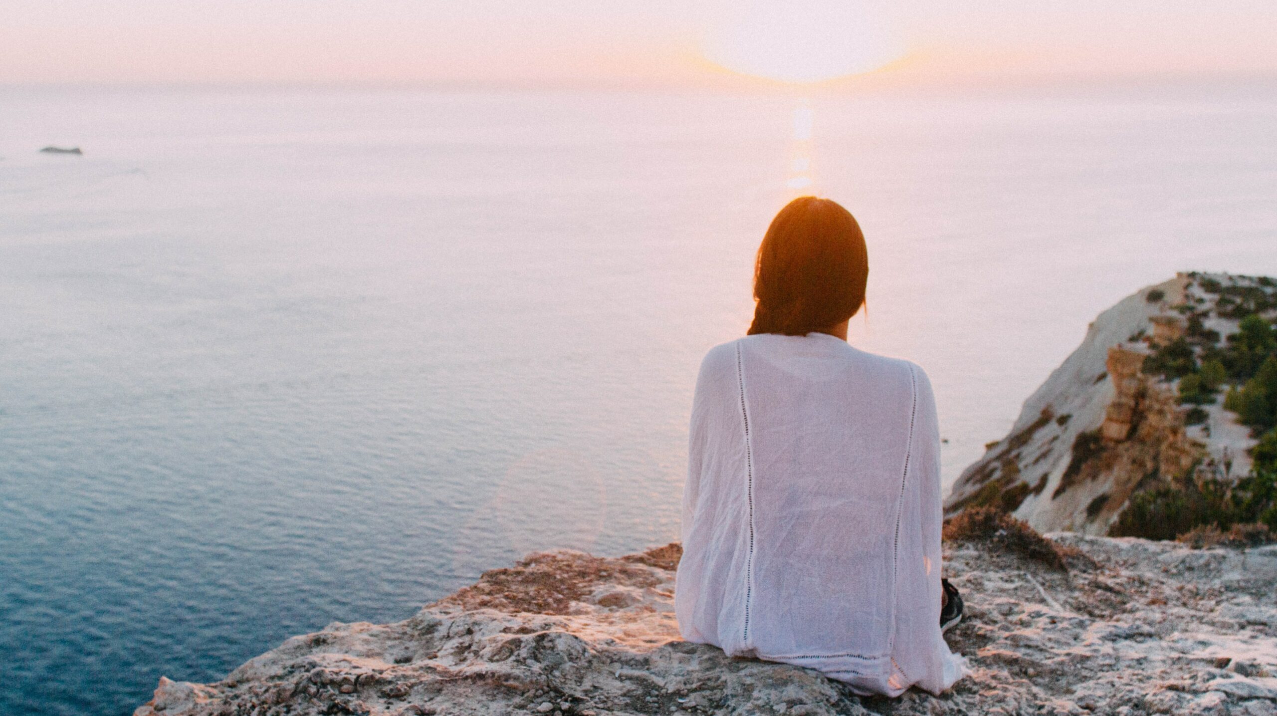 a woman is sitting on a rock looking out at the ocean to represent klonopin addiction risks and faqs.