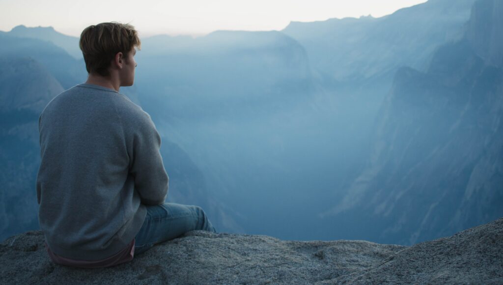 A man sits on a hillside to represent drug abuse and wondering how to tell someone you're an addict. 