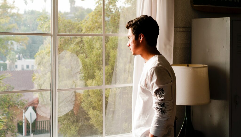 A man stands looking out a window to represent alcohol  detox at home. 