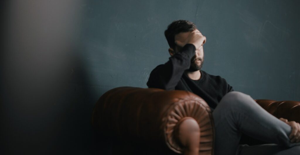 A man sits with his hand on his head to represent kratom addiction and kratom withdrawal. 