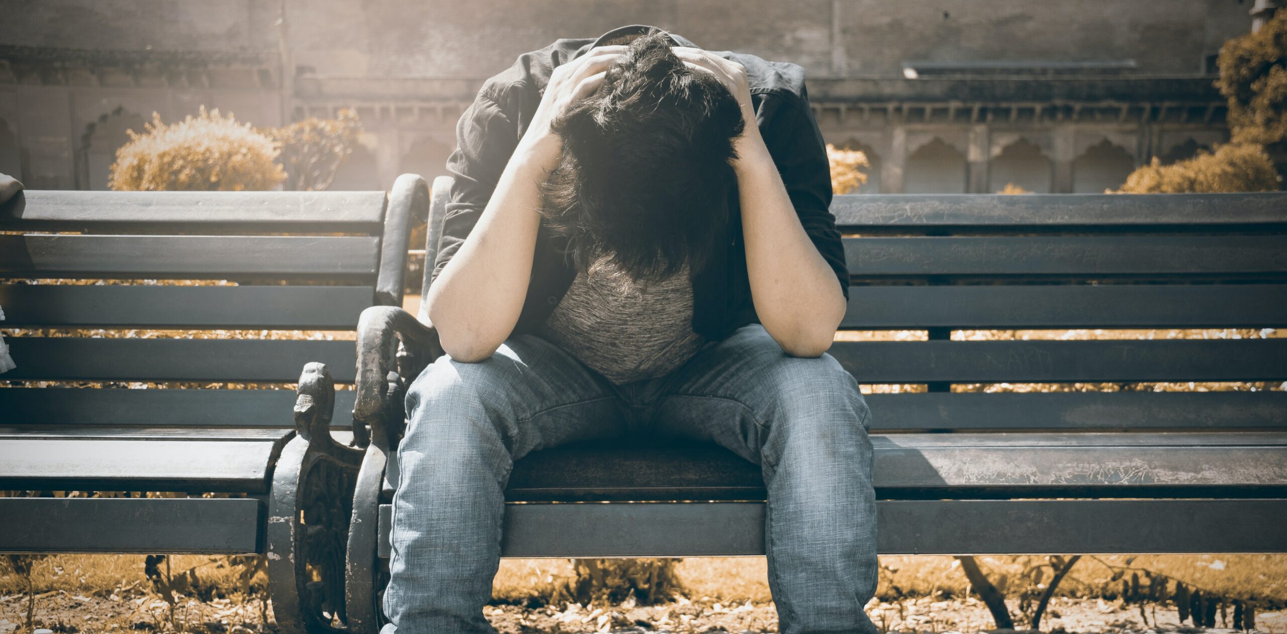 A man sits on a bench with his head down to represent crack cocaine addiction and rehab.