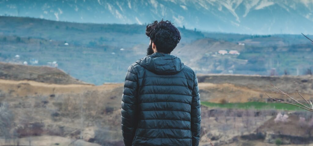 A man stands on a hill looking out at the scenery to represent the disease of addiction. 