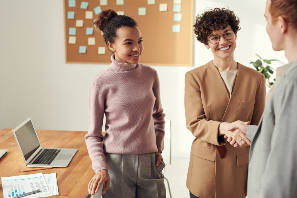 2 people shaking hands at a meeting as a 3rd person stands off to the side looking in