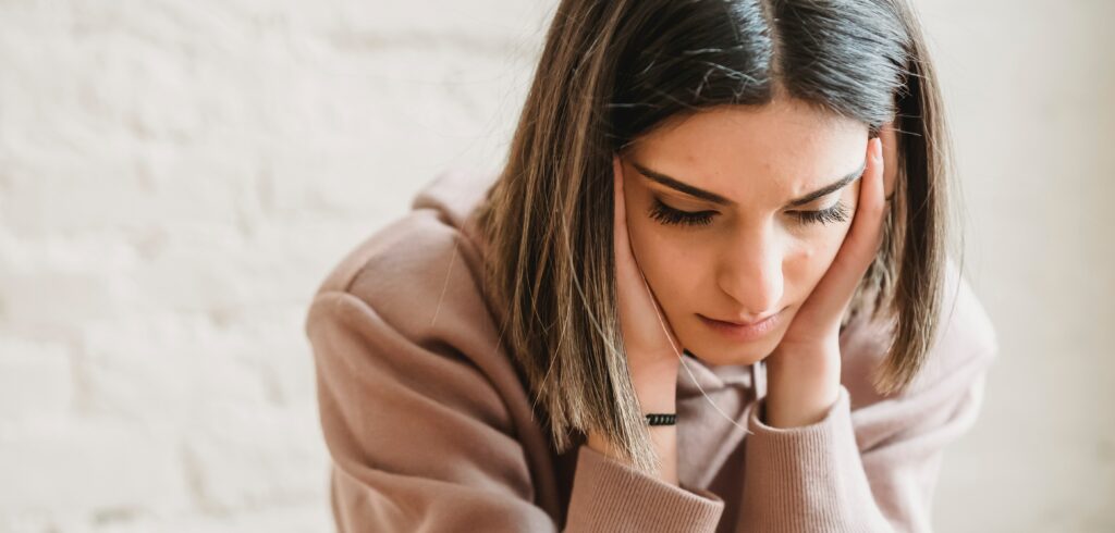 A woman sits with her hands on her face representing how long does dxm take to kick in