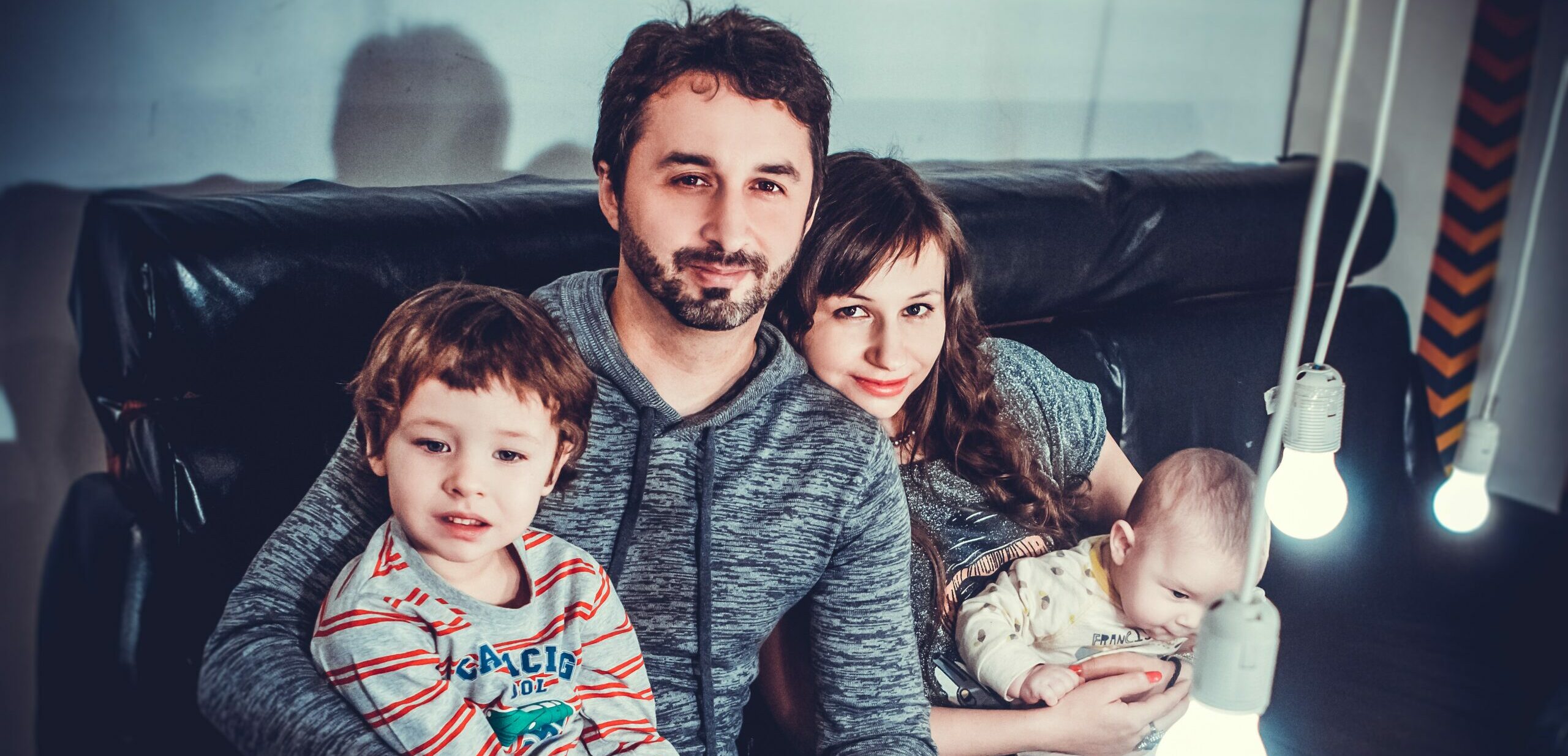 Family of 4: child, father, mother, and baby together on the couch