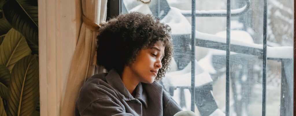 Woman sitting by window representing alcohol addiction symptoms