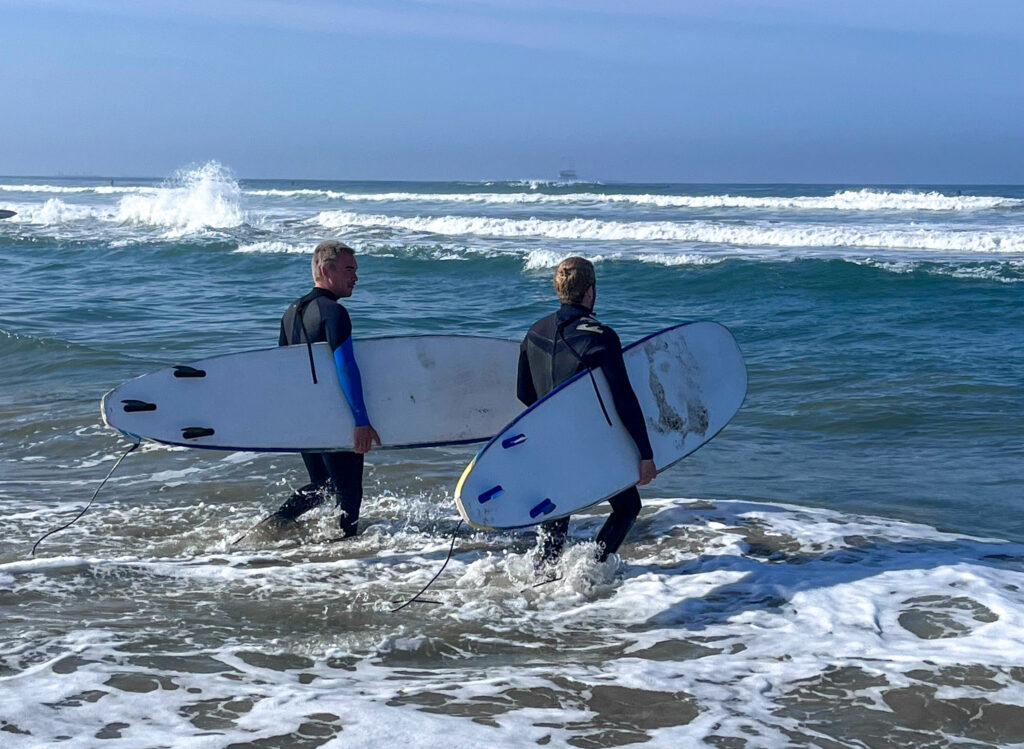 2 surfers walking into the ocean with their surf boards